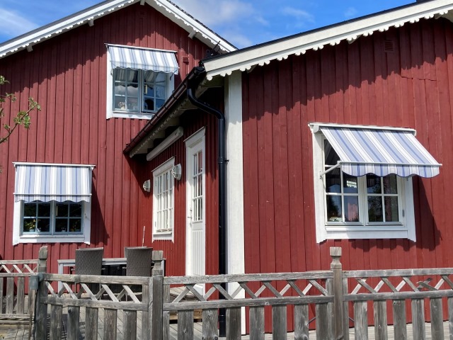 Tre randiga blåa fönstermarkiser på en faluröd villafasad