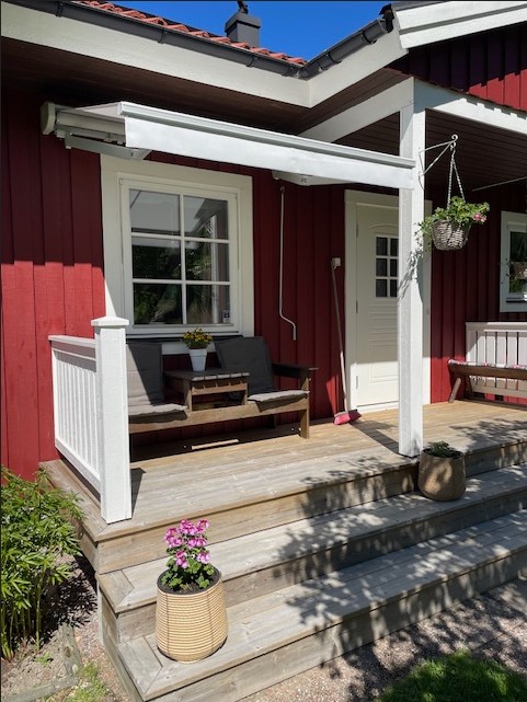 Liten ljus terrassmarkis över farstukvist på rödmålad villa.